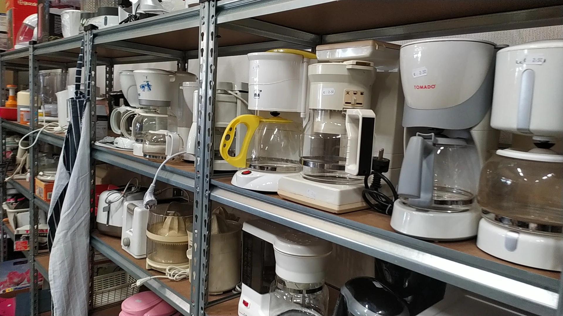 Metalen stellingen met diverse keukenapparaten: koffiezetapparaten, citruspers, mixer en andere huishoudelijke apparatuur
