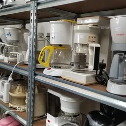 Metalen stellingen met diverse keukenapparaten: koffiezetapparaten, citruspers, mixer en andere huishoudelijke apparatuur