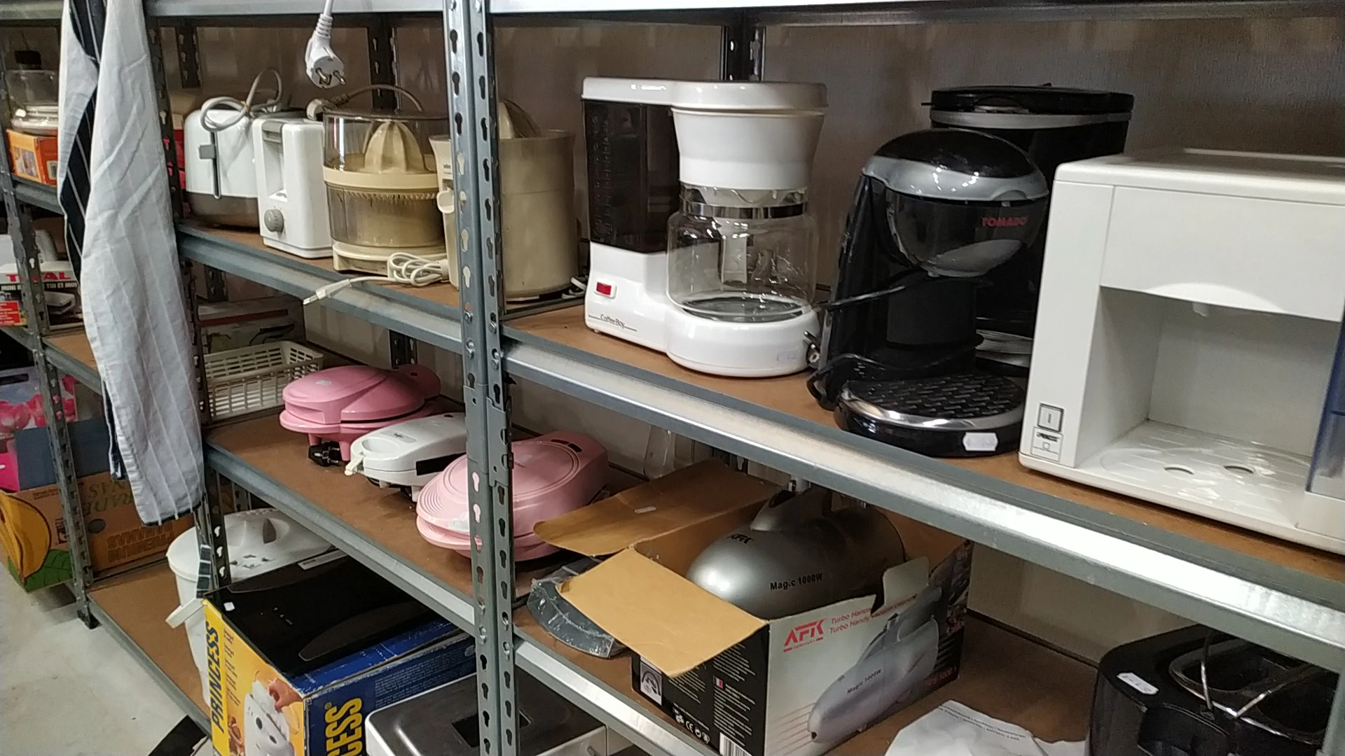Stellingkasten met huishoudelijke apparaten en kitchenware zoals koffiezetapparaten, roze serviesgoed en dozen