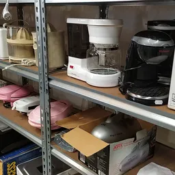 Stellingkasten met huishoudelijke apparaten en kitchenware zoals koffiezetapparaten, roze serviesgoed en dozen