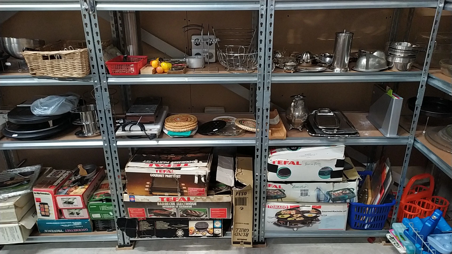 Metalen stellingen vol huishoudelijke artikelen, keukengerei, borden, pannen en overige gebruiksvoorwerpen
