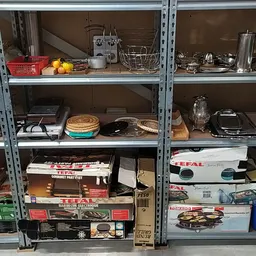 Metalen stellingen vol huishoudelijke artikelen, keukengerei, borden, pannen en overige gebruiksvoorwerpen