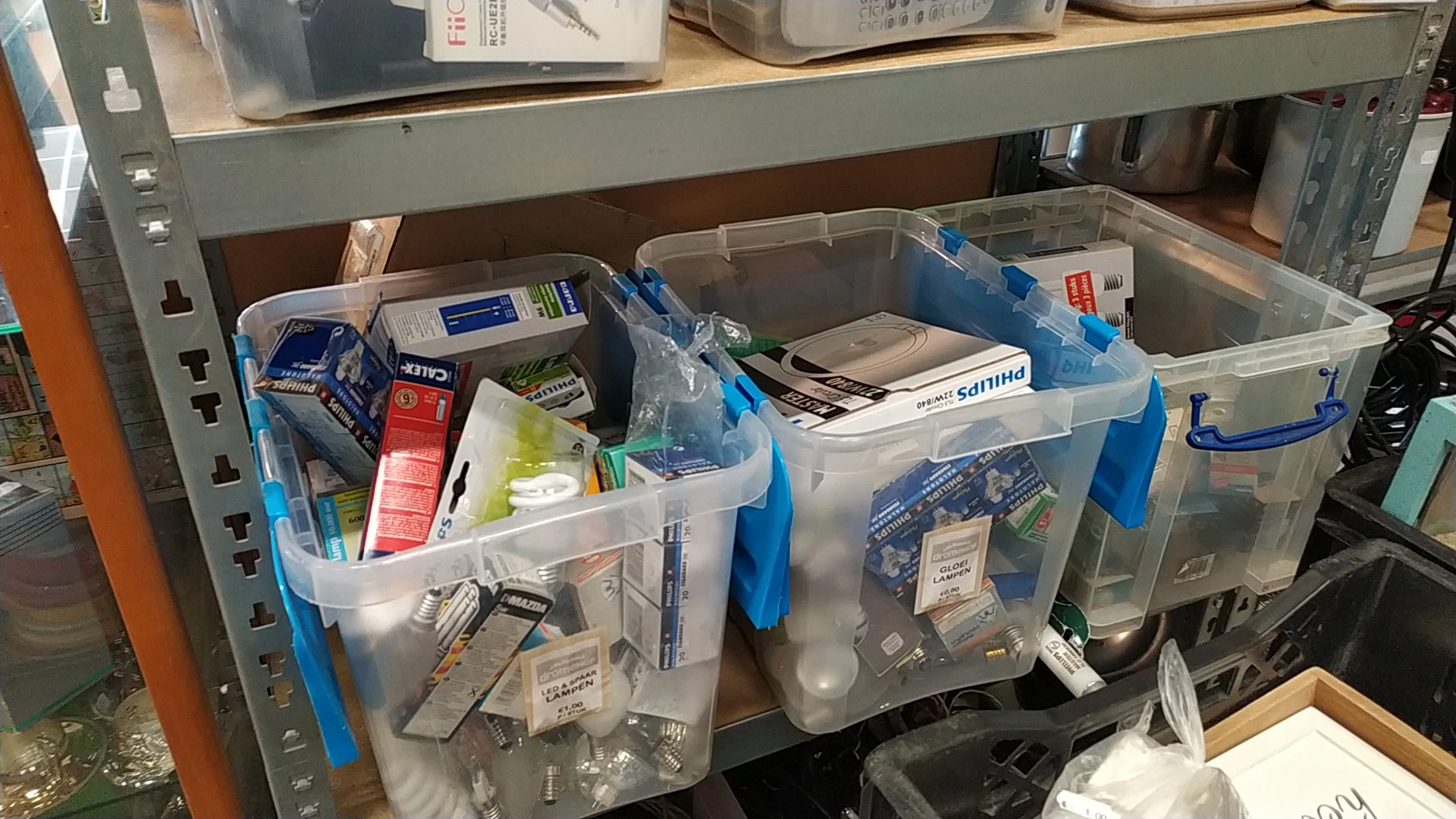 Plastic opbergboxen met blauwe handvaten gevuld met diverse artikelen op een plank