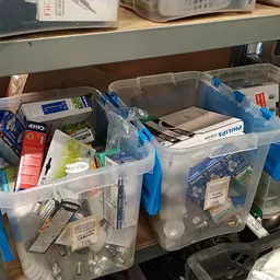 Plastic opbergboxen met blauwe handvaten gevuld met diverse artikelen op een plank