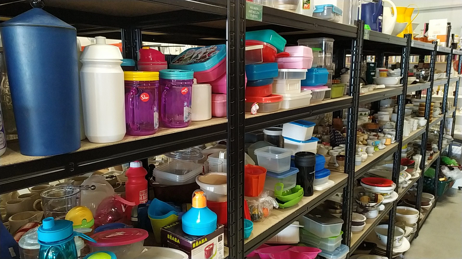 Stellingen met plastic bakken, doosjes en opbergcontainers in verschillende kleuren en maten