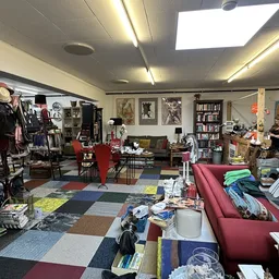 Winkelvloer met kleding op rekken, rode meubels, boekenkasten en diverse tweedehands spullen