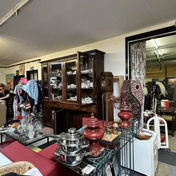 Interieur van kringloopwinkel met donkerhouten vitrinekast, rood servies en decoratieve items op toonbank