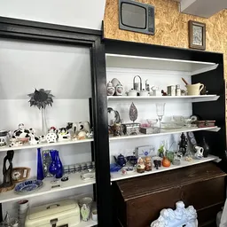 Twee zwarte kasten met witte en zwarte planken vol met decoratieve items, servies, beeldjes en huishoudartikelen