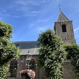 Historische kerk met toren, klimop en bloemen tegen blauwe hemel