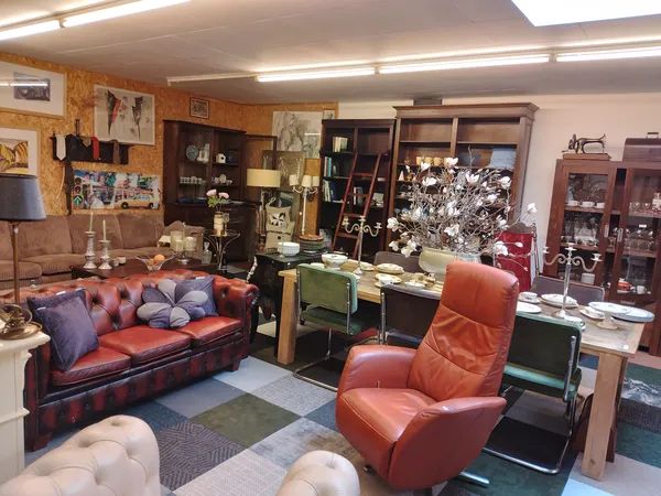 Winkelinterieur met rode leren bank, oranje fauteuil, houten kasten, boekenplanken en diverse meubels en decoraties