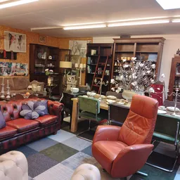Winkelinterieur met rode leren bank, oranje fauteuil, houten kasten, boekenplanken en diverse meubels en decoraties