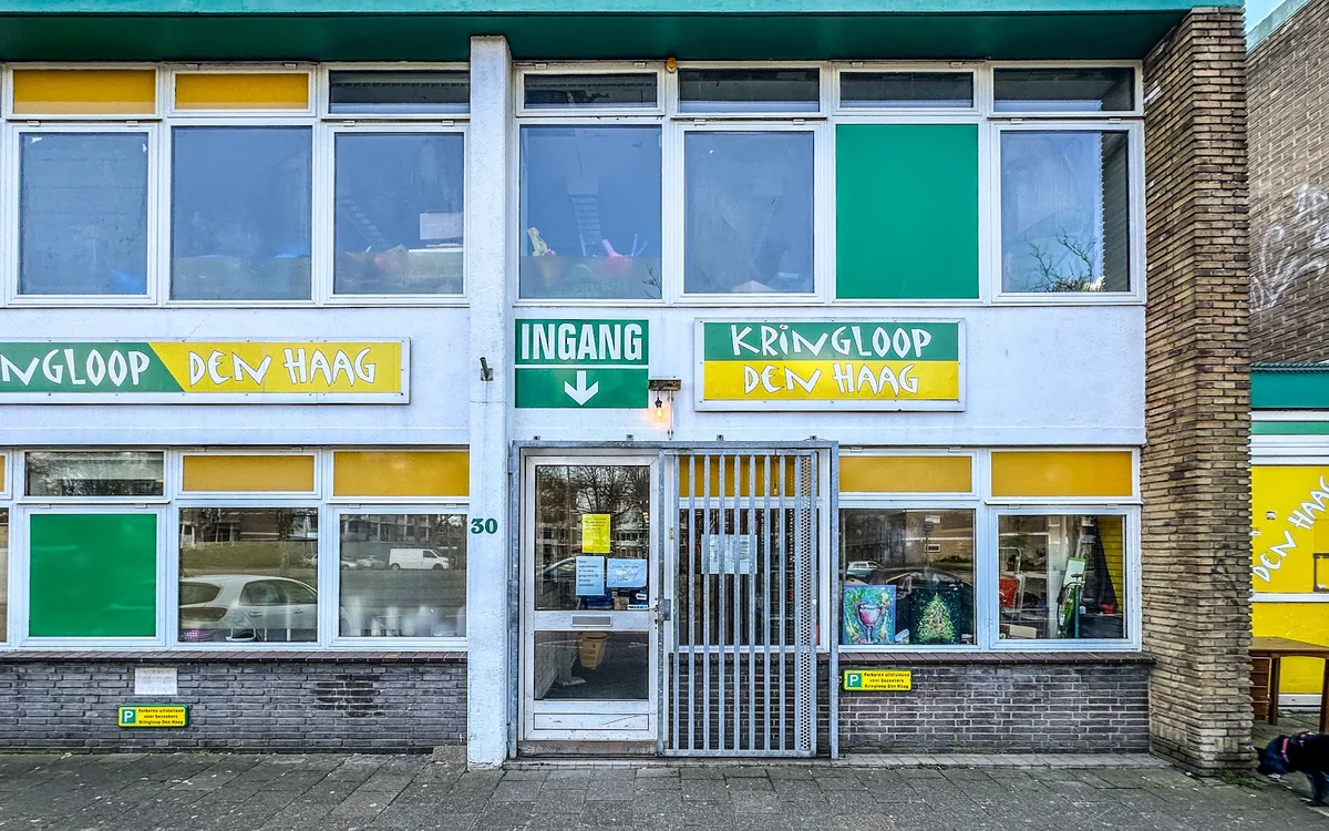 Gevel van kringloopwinkel met geel-groen design, grote ramen en ingang op straatniveau