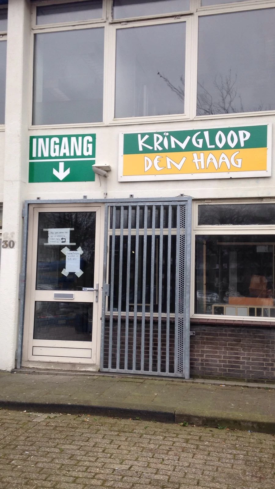 Ingang van kringloopwinkel met groene pijl en gesloten deur met spijlen