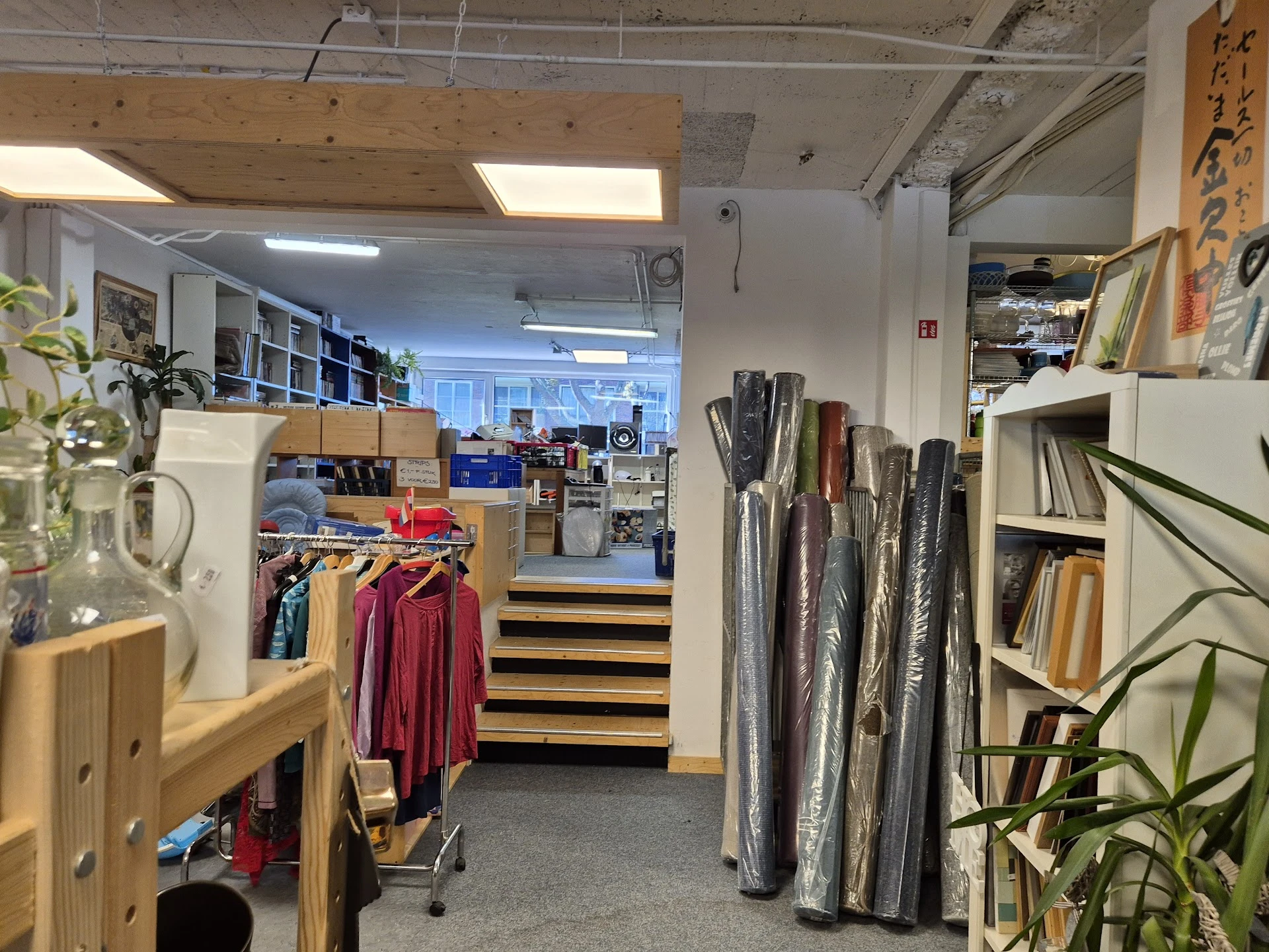 Winkelvloer met houten stellingen, kleding op hangers, uitgestalde stoffenrollen en plantendecoratie