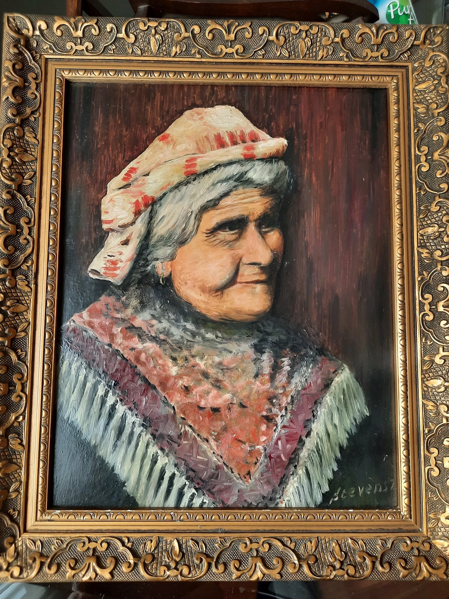 Schilderij van een oudere vrouw met grijze haren, roze en rood geborduurde muts en rode kraag in gouden lijst