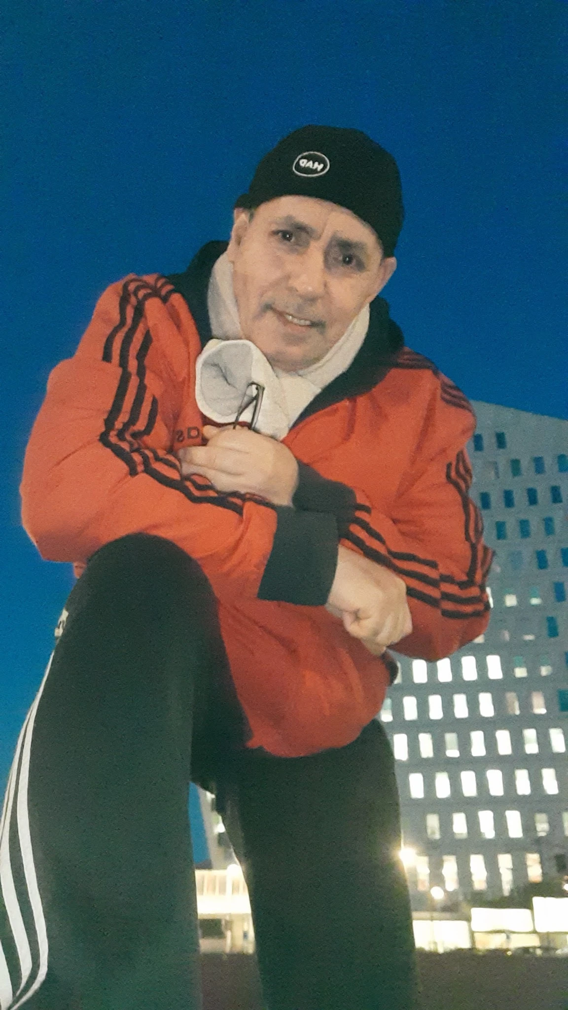 Close-up van een rood Adidas-jack met zwarte strepen, gedragen door een persoon tegen blauwe achtergrond