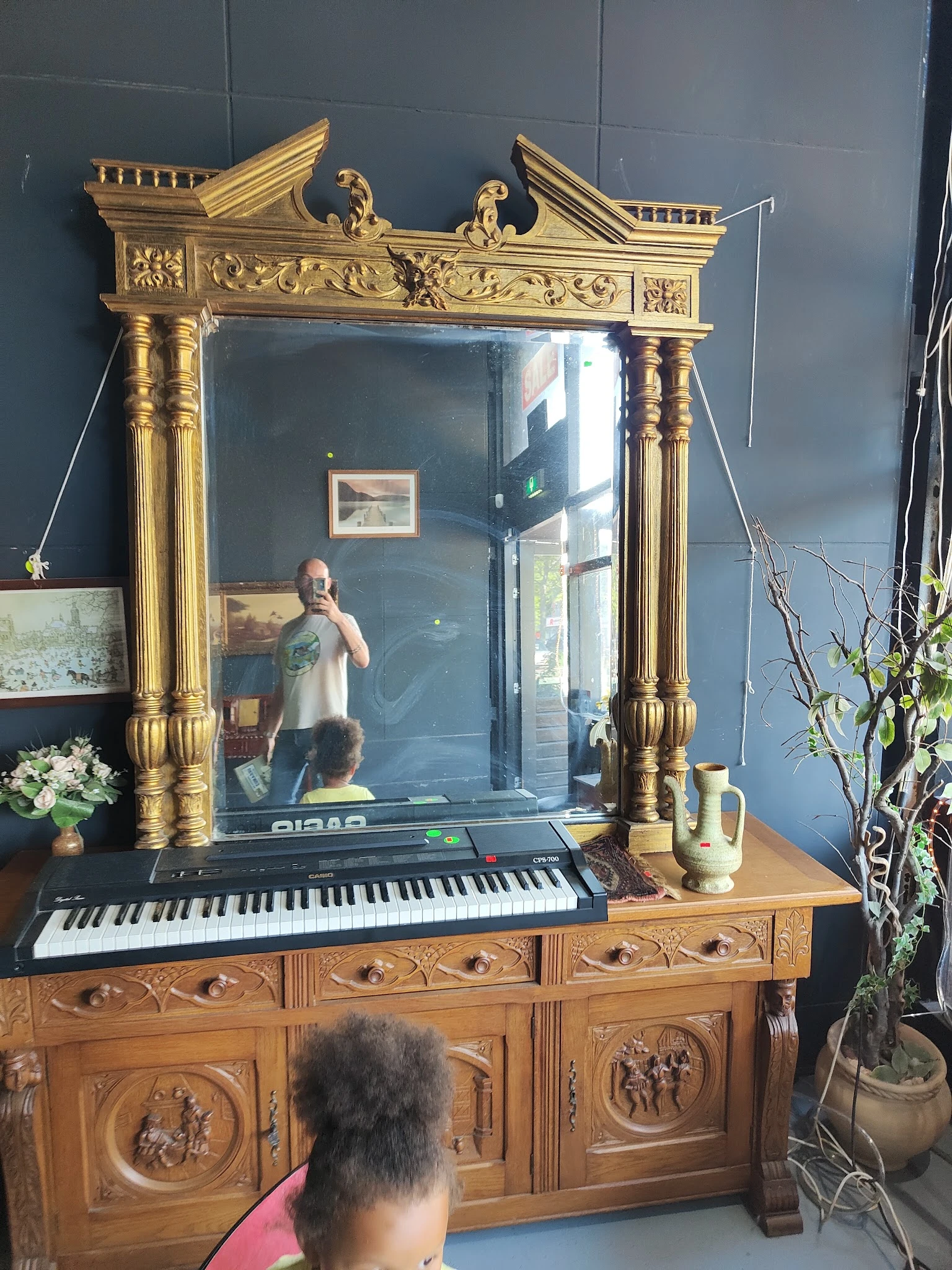 Gouden spiegellijst met decoratieve zuilen boven houten commode met keyboard, tegen blauwe muur