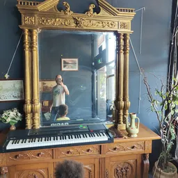 Gouden spiegellijst met decoratieve zuilen boven houten commode met keyboard, tegen blauwe muur