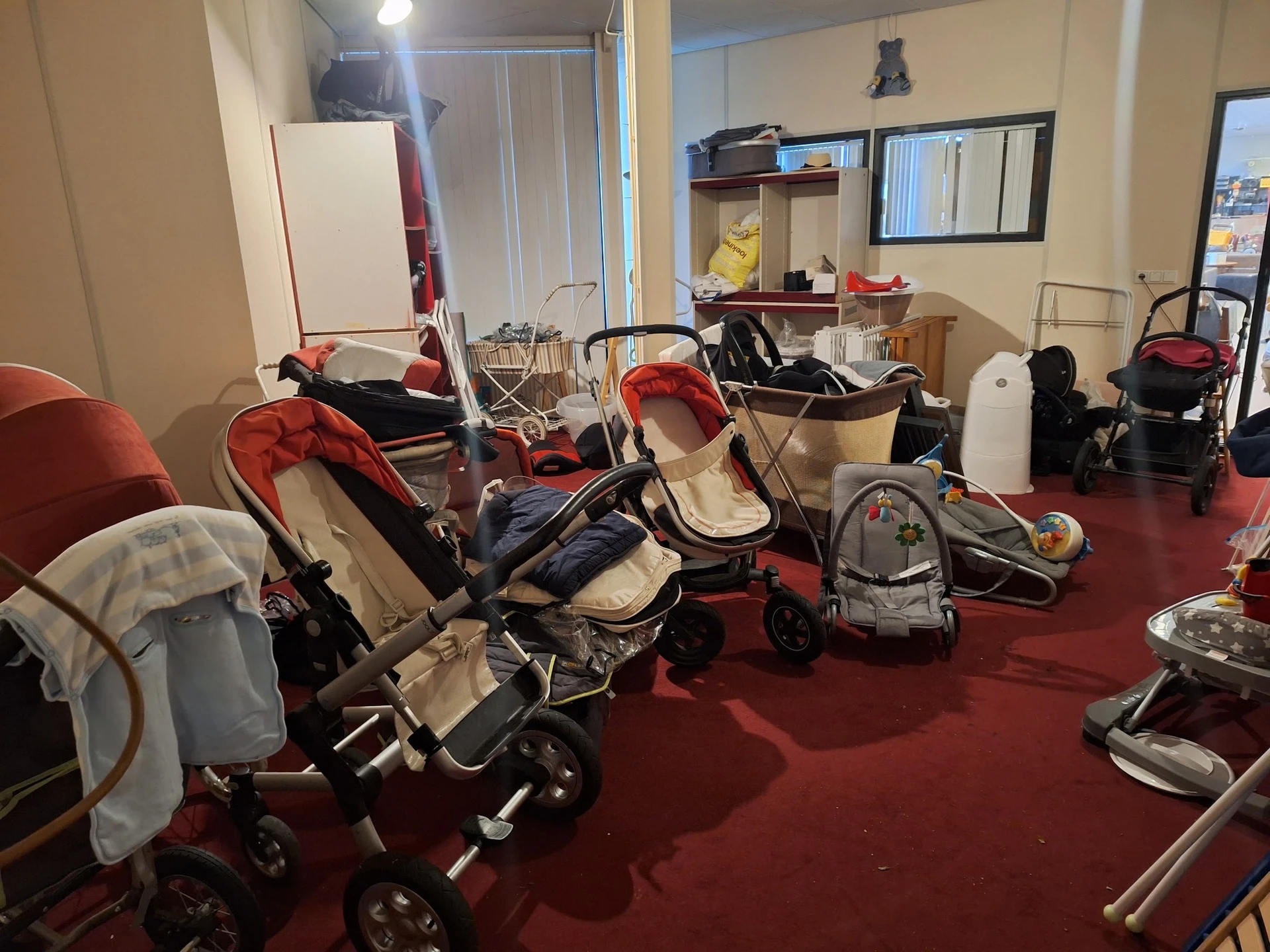 Meerdere kinderwagens en buggy's uitgestald in een ruimte met rode vloer