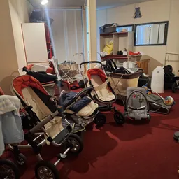 Meerdere kinderwagens en buggy's uitgestald in een ruimte met rode vloer