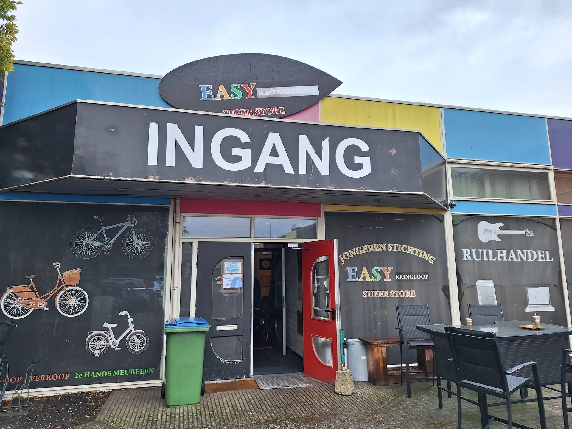 Gevel van kringloopwinkel Easy met ingang, zwarte pui met fietsen afgebeeld, gekleurde bovenkant