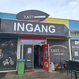 Gevel van kringloopwinkel Easy met ingang, zwarte pui met fietsen afgebeeld, gekleurde bovenkant