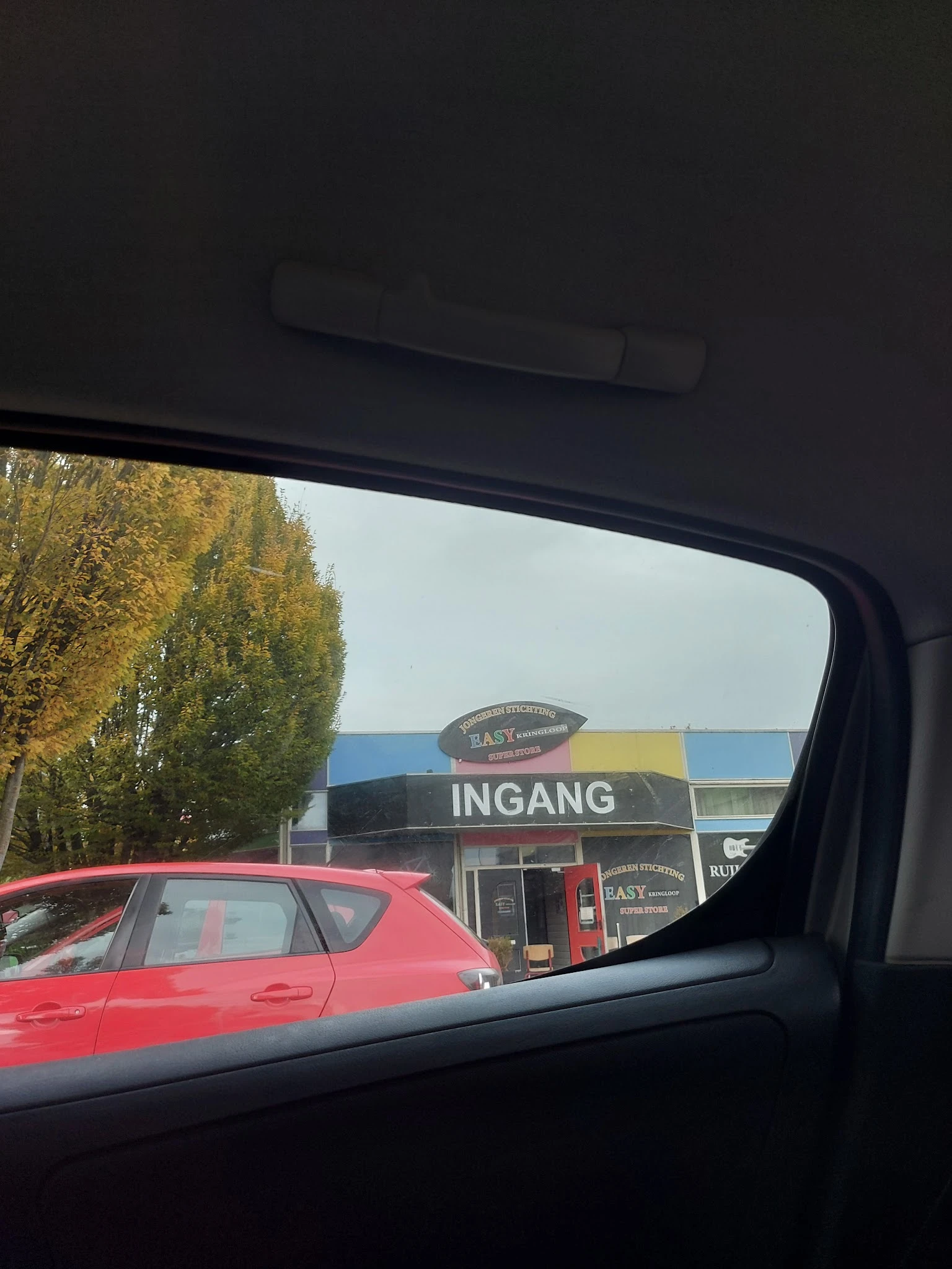 Winkelgevel met 'INGANG' opschrift gezien vanuit auto, deels verborgen door voertuig op voorgrond
