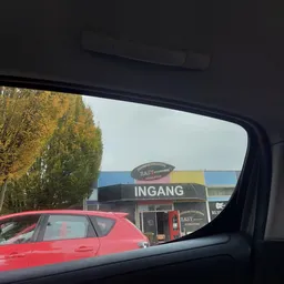 Winkelgevel met 'INGANG' opschrift gezien vanuit auto, deels verborgen door voertuig op voorgrond