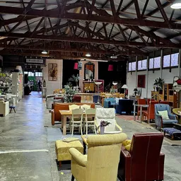 Ruim interieur van kringloopwinkel met diverse meubels: stoelen, tafels, kasten en decorstukken uitgestald.