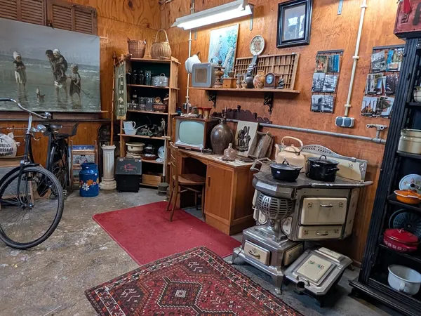 Winkelvloer met vintage huishoudapparatuur, meubels, televisies en decoratieartikelen op houten planken tegen houten wanden