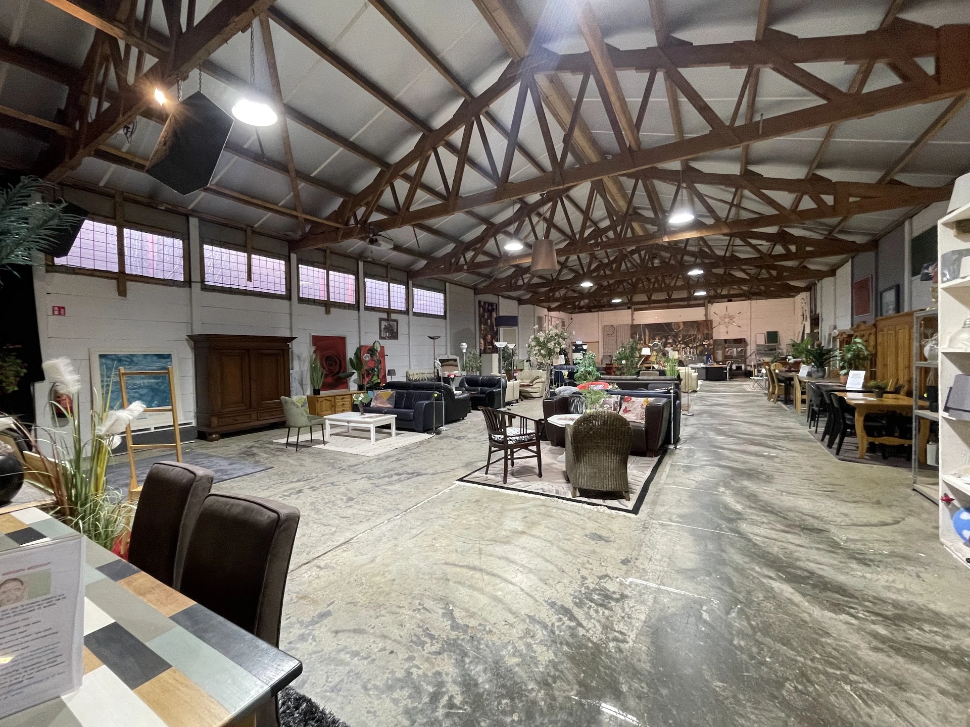 Ruim kringloopcentrum met houten dakconstructie, diverse meubels en spullen uitgestald op de vloer