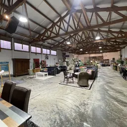 Ruim kringloopcentrum met houten dakconstructie, diverse meubels en spullen uitgestald op de vloer