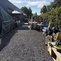 Terras met tafels, stoelen en parasols buiten een winkel met groene hagen