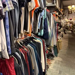 Rekken met tweedehands kleding op hangers in de winkel, diverse kleuren en kledingstukken