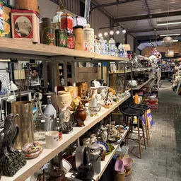Tafel met diverse decoratieve items zoals beeldjes, vazen, kandelaren en andere huishoudelijke spullen in tweedehands winkel