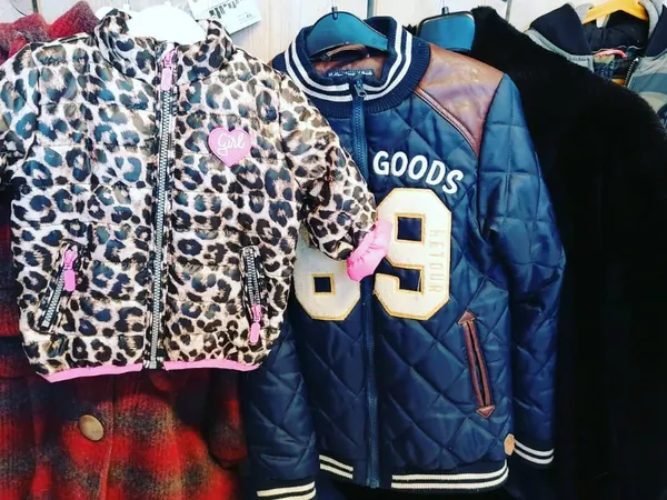 Rekken met tweedehands kinderkleding: een luipaardprint vest, een blauw sportief jack en zwarte kledingstukken.