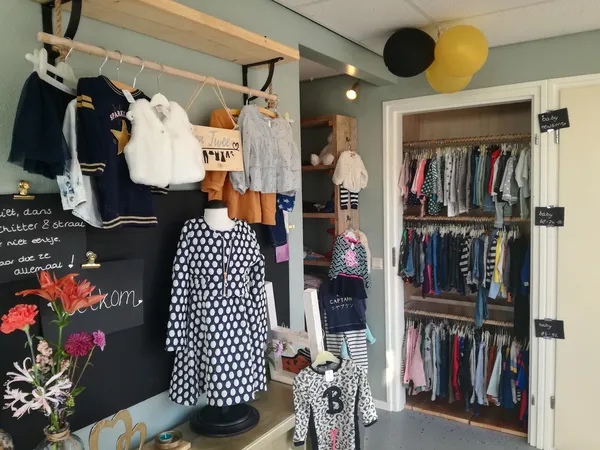 Winkelinterieur met kinderkleding op hangers, stellingen met kleding en decoratieve elementen zoals ballonnen