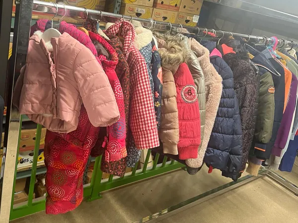 Rekken met tweedehands kinderkleding, waaronder roze en rood gewatteerde jassen en jasjes