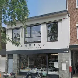 Witte gevel van kringloopwinkel Emmaus Bilthoven met grote ramen en donkere winkelpui.