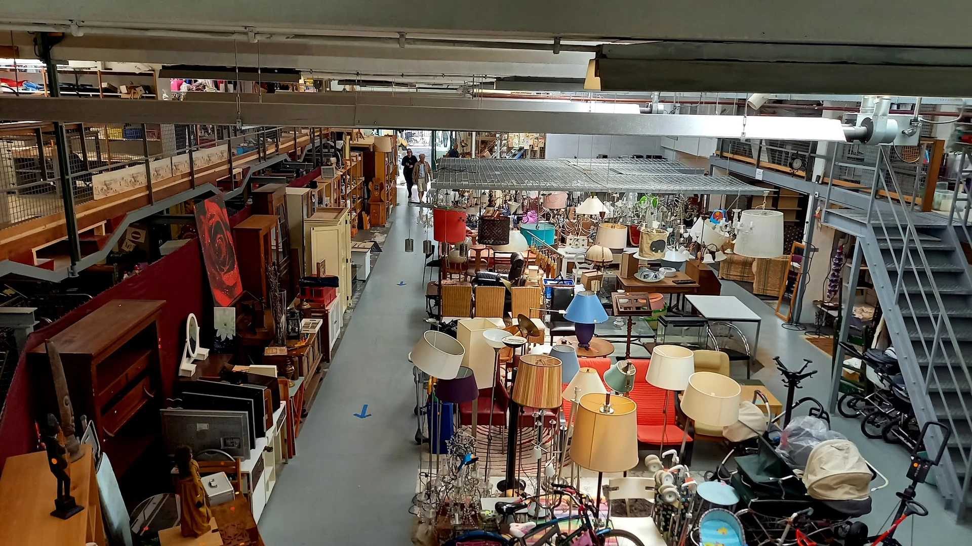 Overzicht van de kringloopwinkel met meubels, lampen en huishoudartikelen op de vloer en stellingen