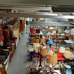 Overzicht van de kringloopwinkel met meubels, lampen en huishoudartikelen op de vloer en stellingen