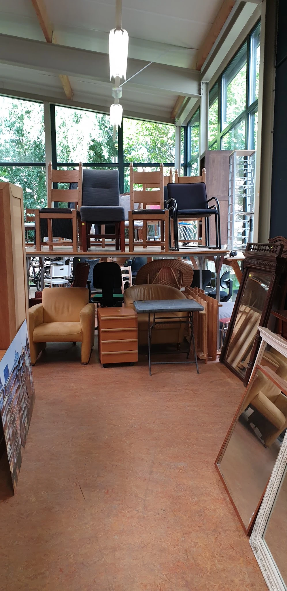 Tweedehands meubels en stoelen in de winkel, waaronder een oranje fauteuil, houten tafels en diverse stoelen.