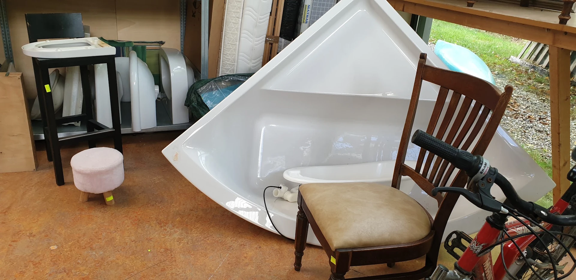 Witte hoekbadkuip en houten stoel met zitting in de winkel