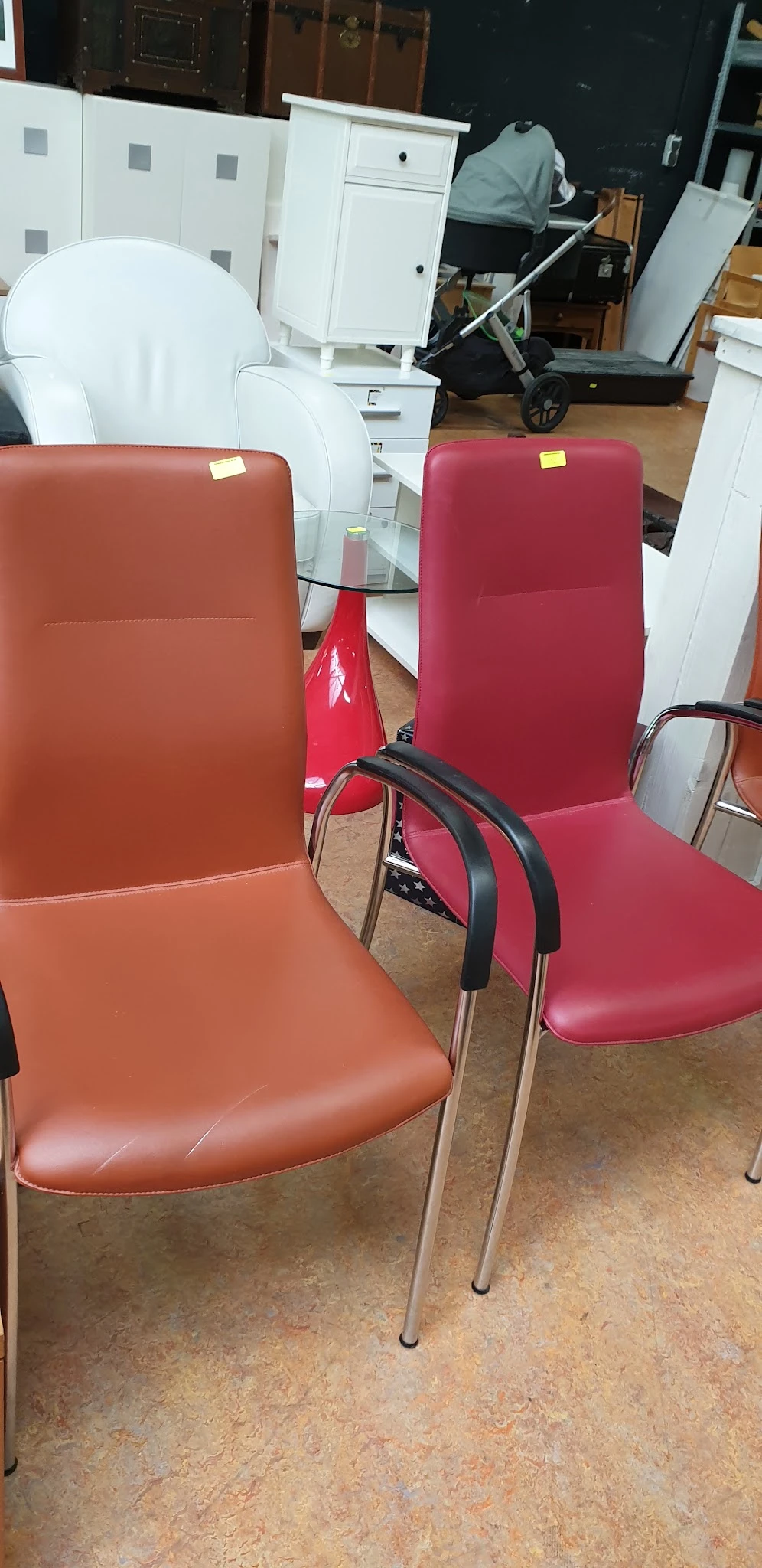 Drie designstoelen met rode en oranje bekleding en zwarte armsteunen in een kringloopwinkel
