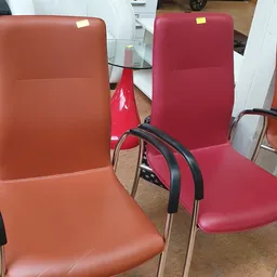 Drie designstoelen met rode en oranje bekleding en zwarte armsteunen in een kringloopwinkel