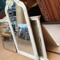 Witte spiegel met decoratieve lijst naast houten meubels in de winkel