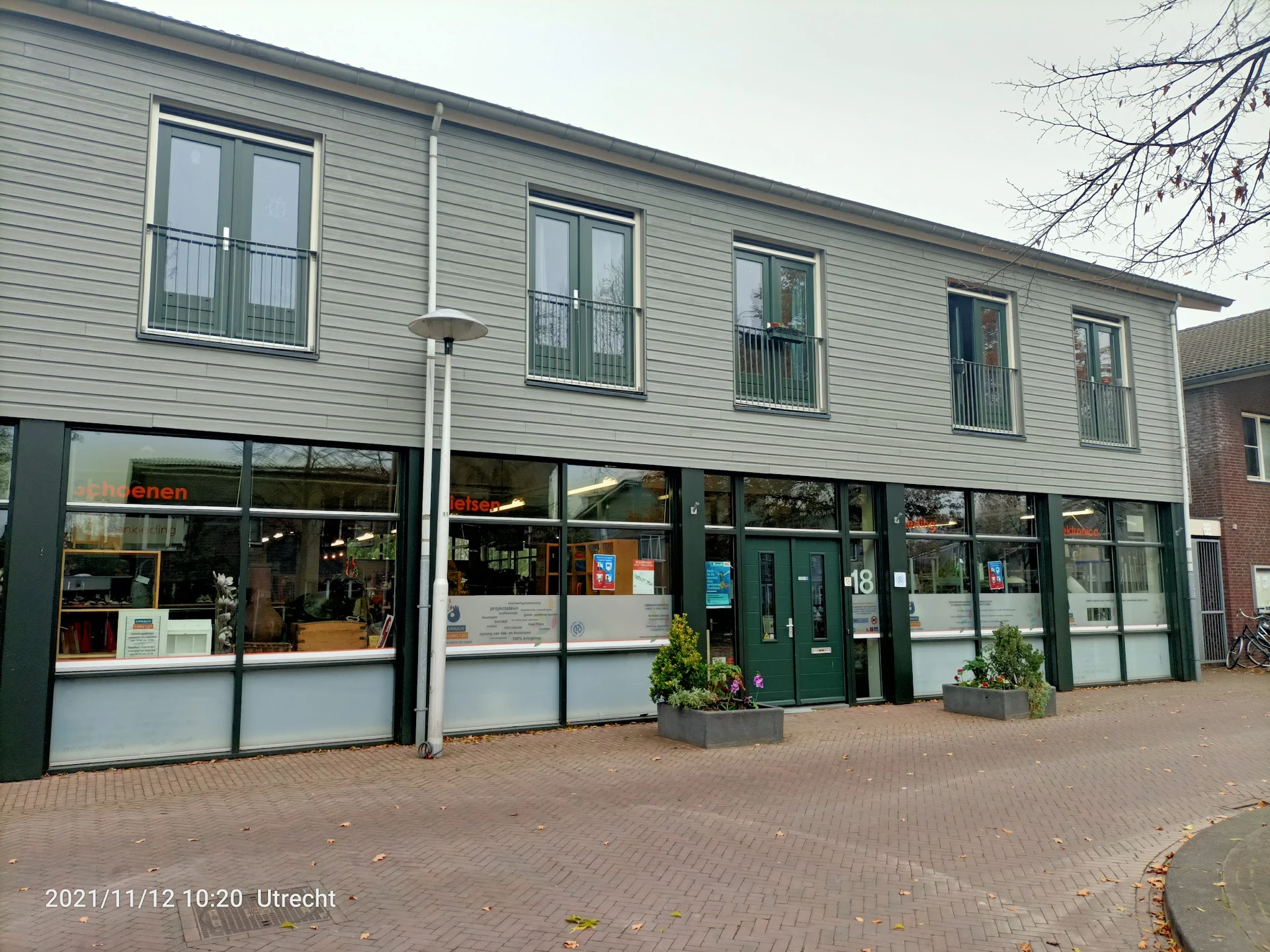 Gevel van kringloopwinkel met groene deuren, grote winkelramen en witte zijwanden, meerdere bovenramen