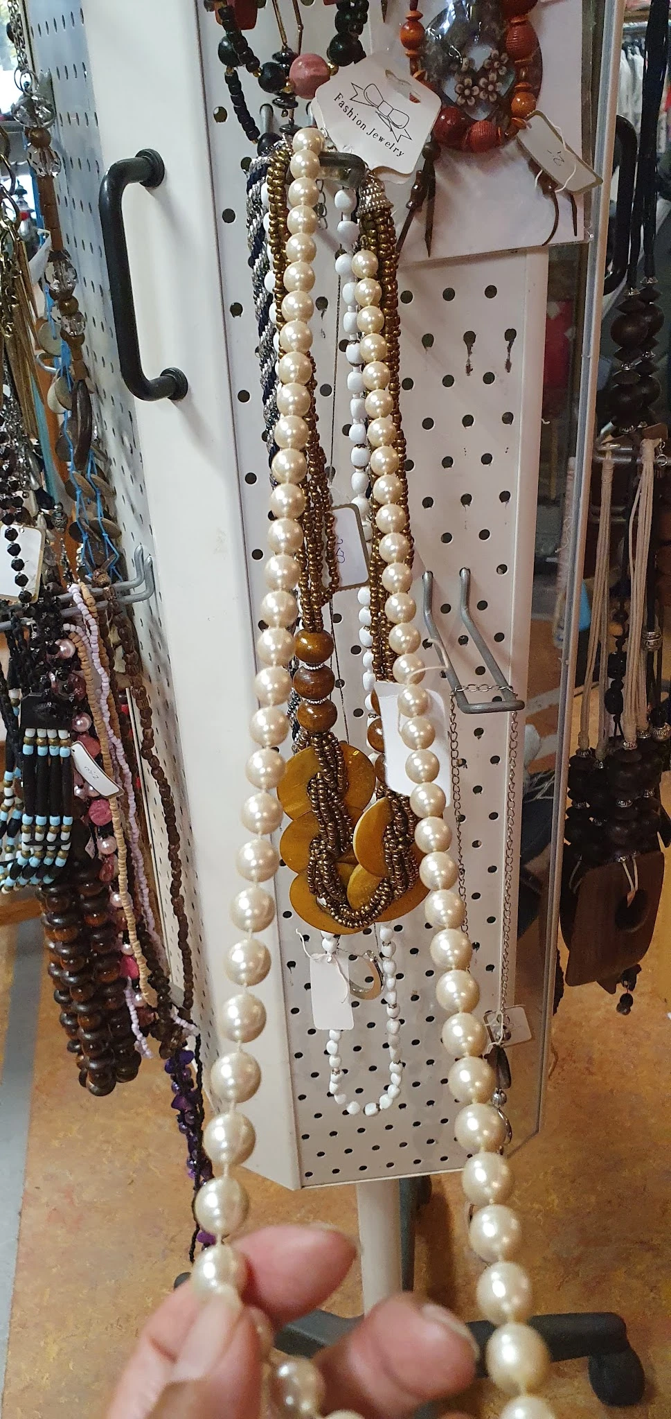 Close-up van sieraden aan een pegboard: parelkettingen met goudkleurige kralen en een goudkleurige hanger.