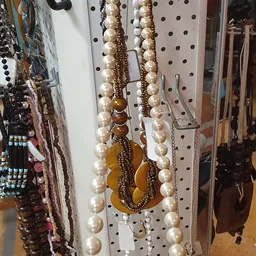 Close-up van sieraden aan een pegboard: parelkettingen met goudkleurige kralen en een goudkleurige hanger.