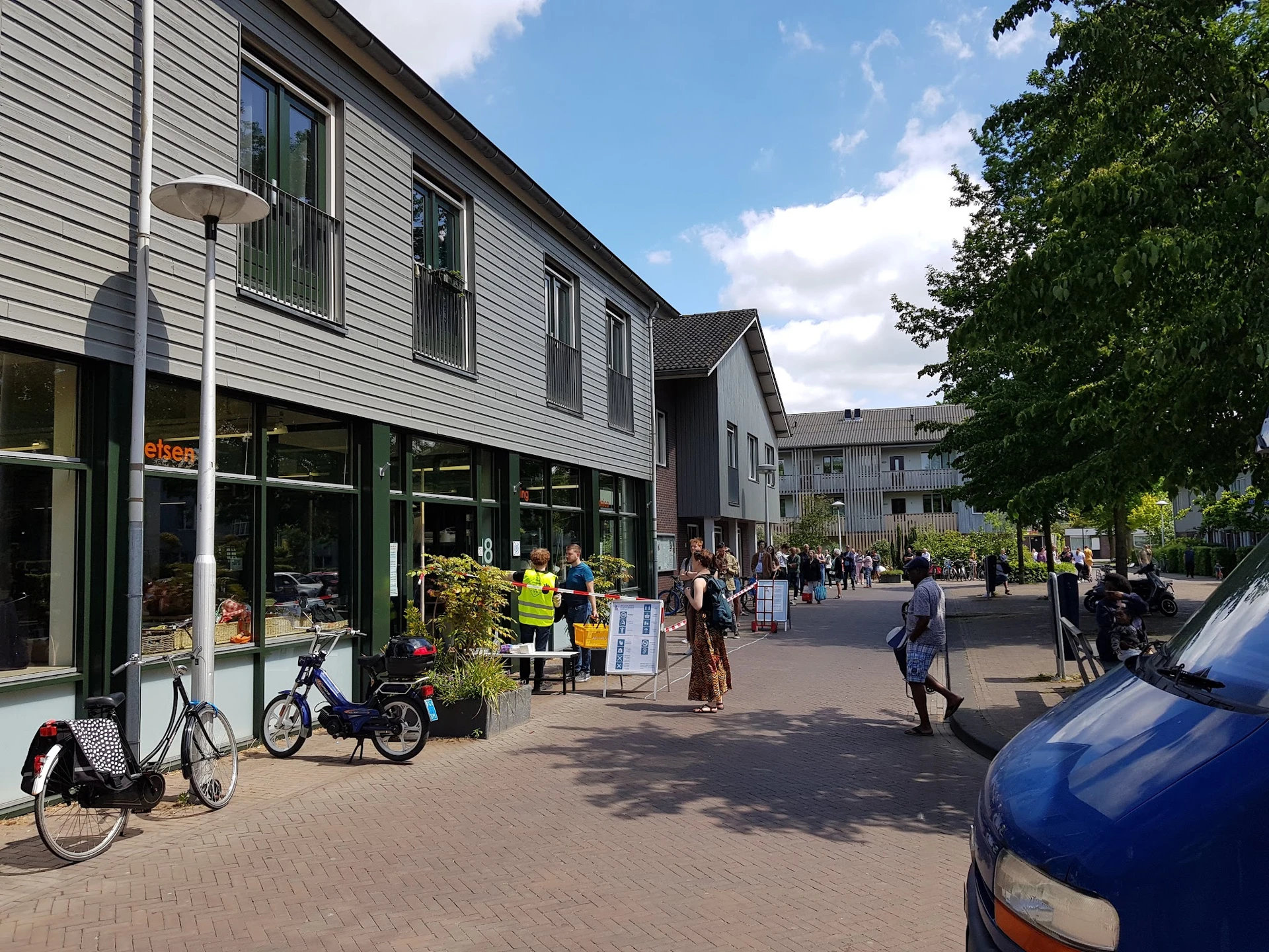 Gevel van kringloopwinkel met grote winkelruit aan een plein met voetgangers en fietsen